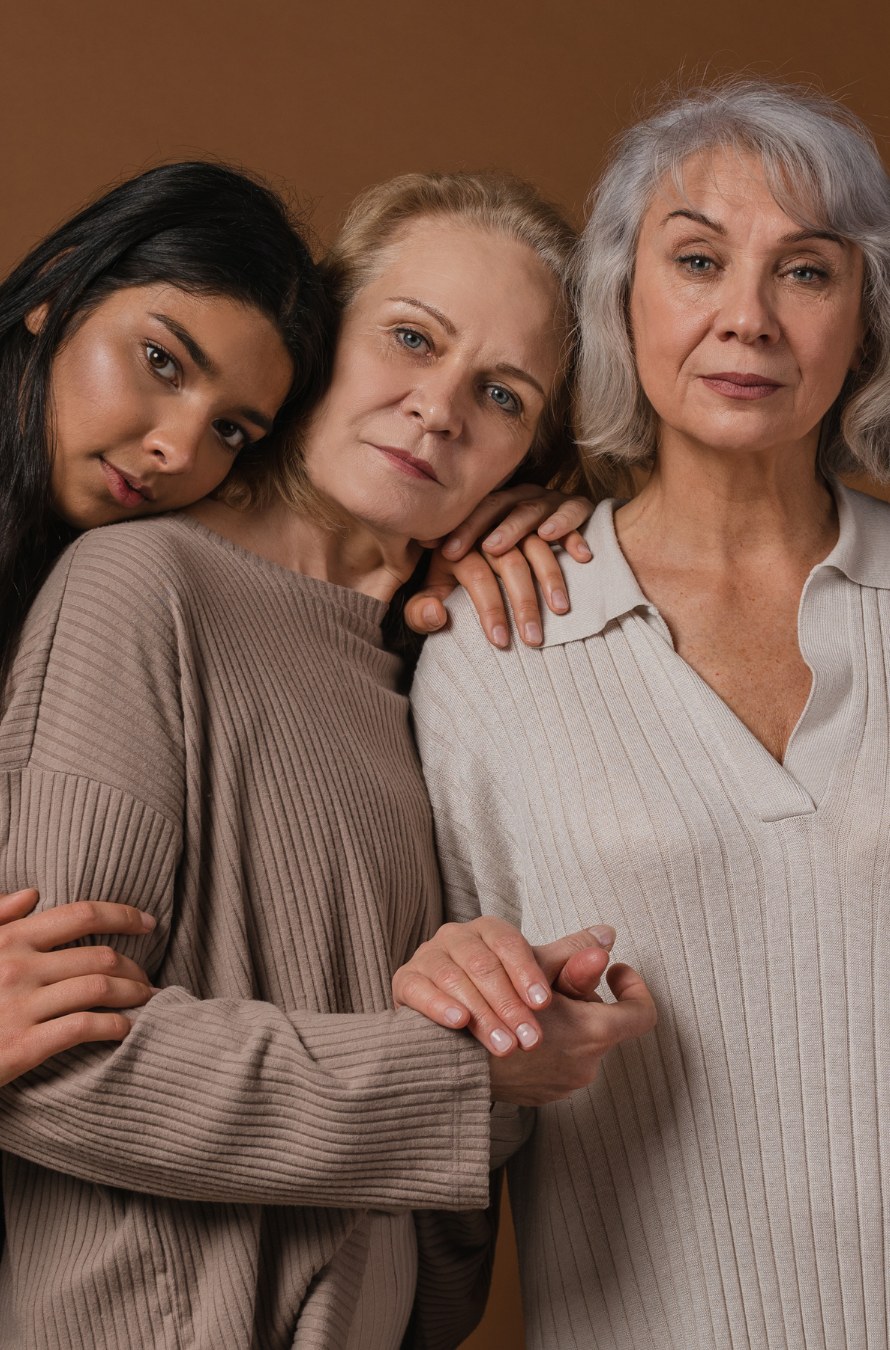 Three women of different ages leaning on one another, looking towards the camera.
